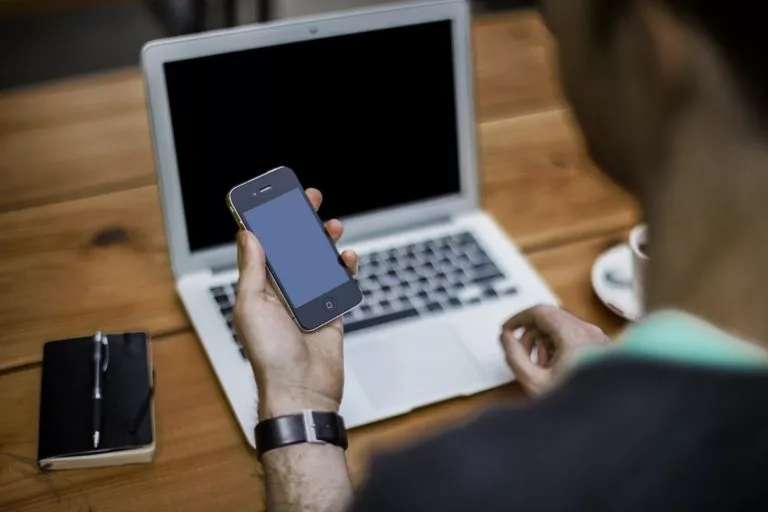 Osoba trzymająca telefon przed laptopem